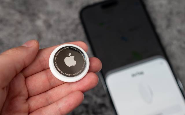 In womans hand small AirTag Apple, on background out of focus smartphone which are connected to tag. Air Tag gadget to track of your stuff.